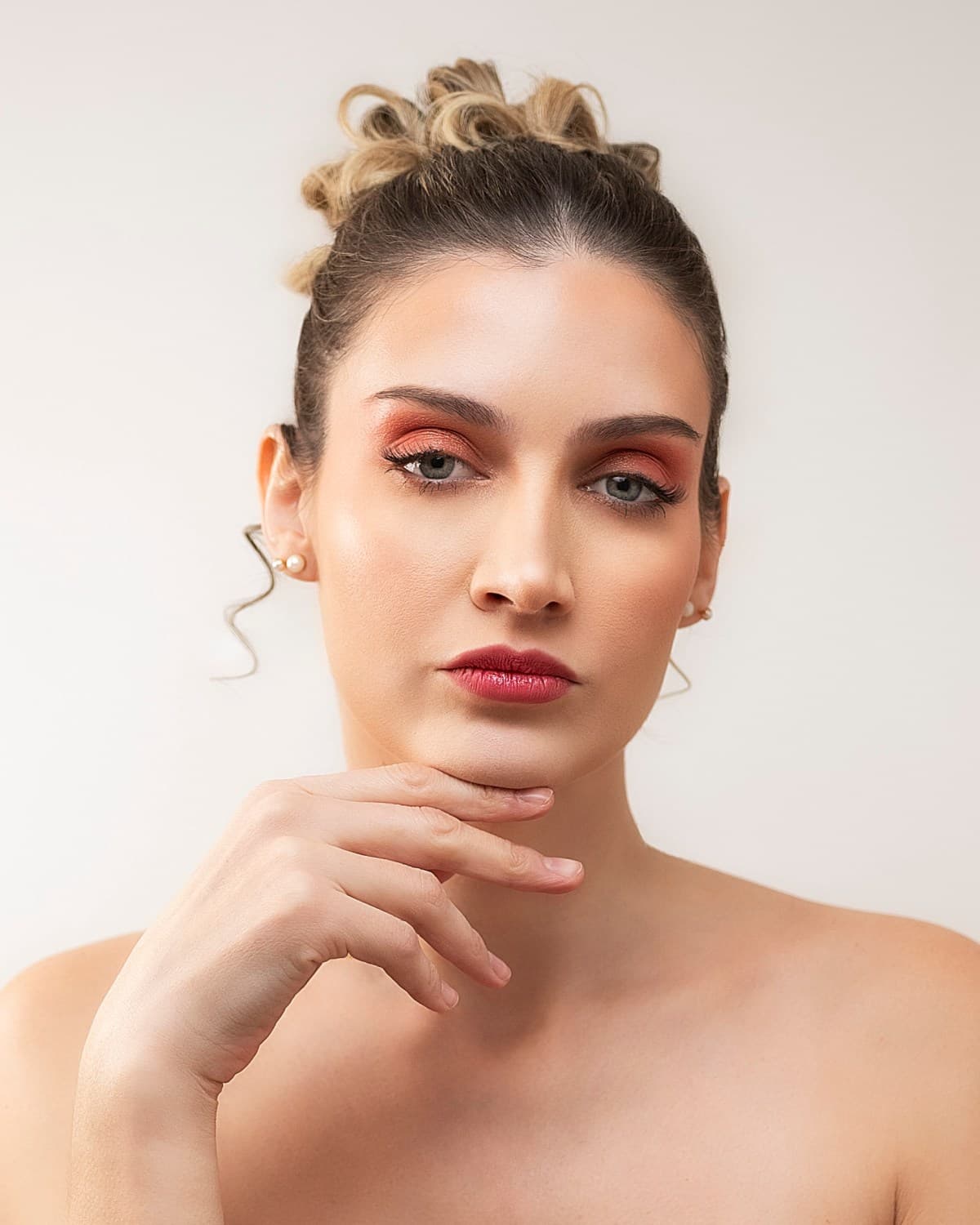 Retrato de beauty con sombra en tonos rojizos, mano cerca del rostro sobre fondo claro