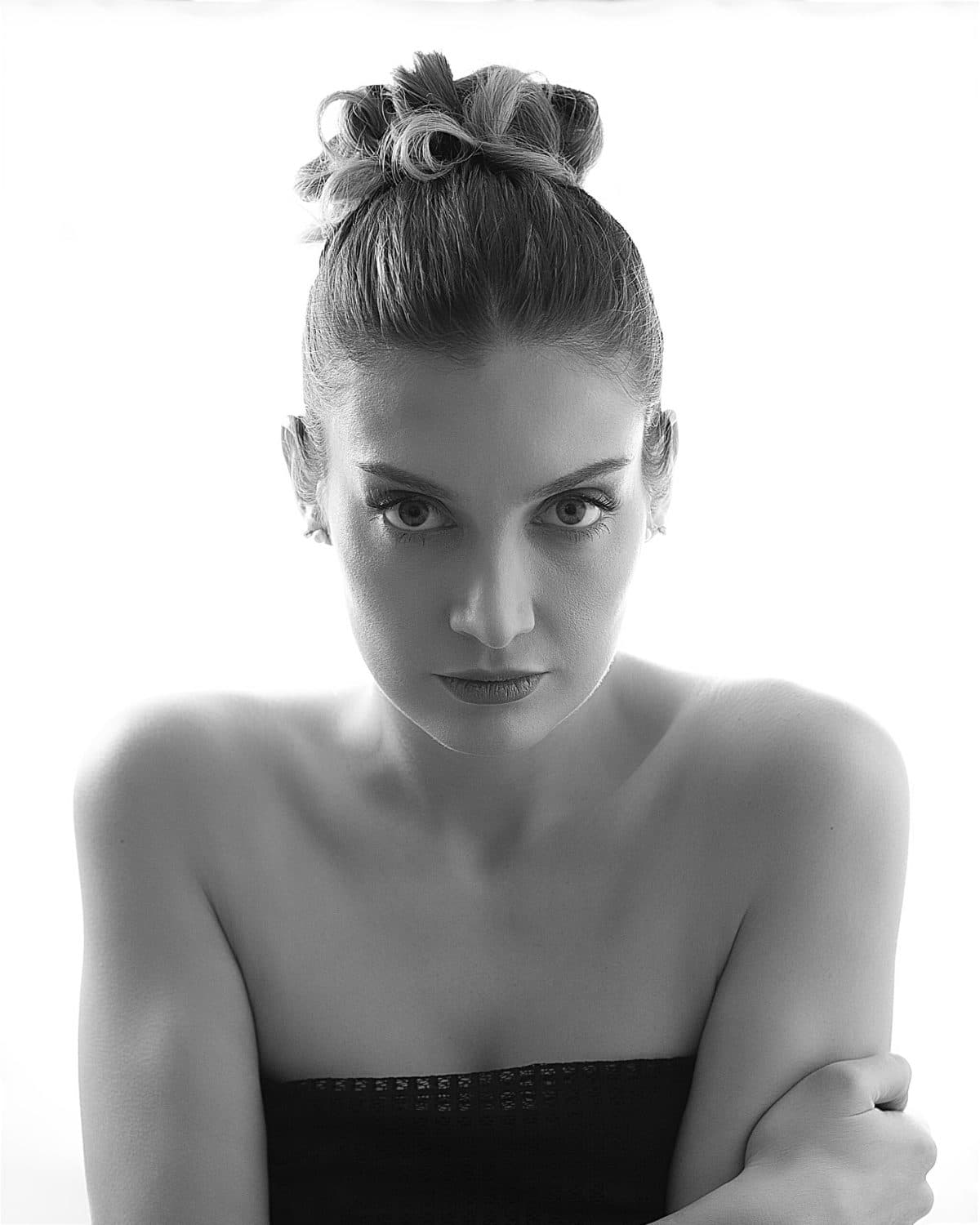 Retrato de beauty con la mano bajo el mentón, mirada lateral sobre fondo claro